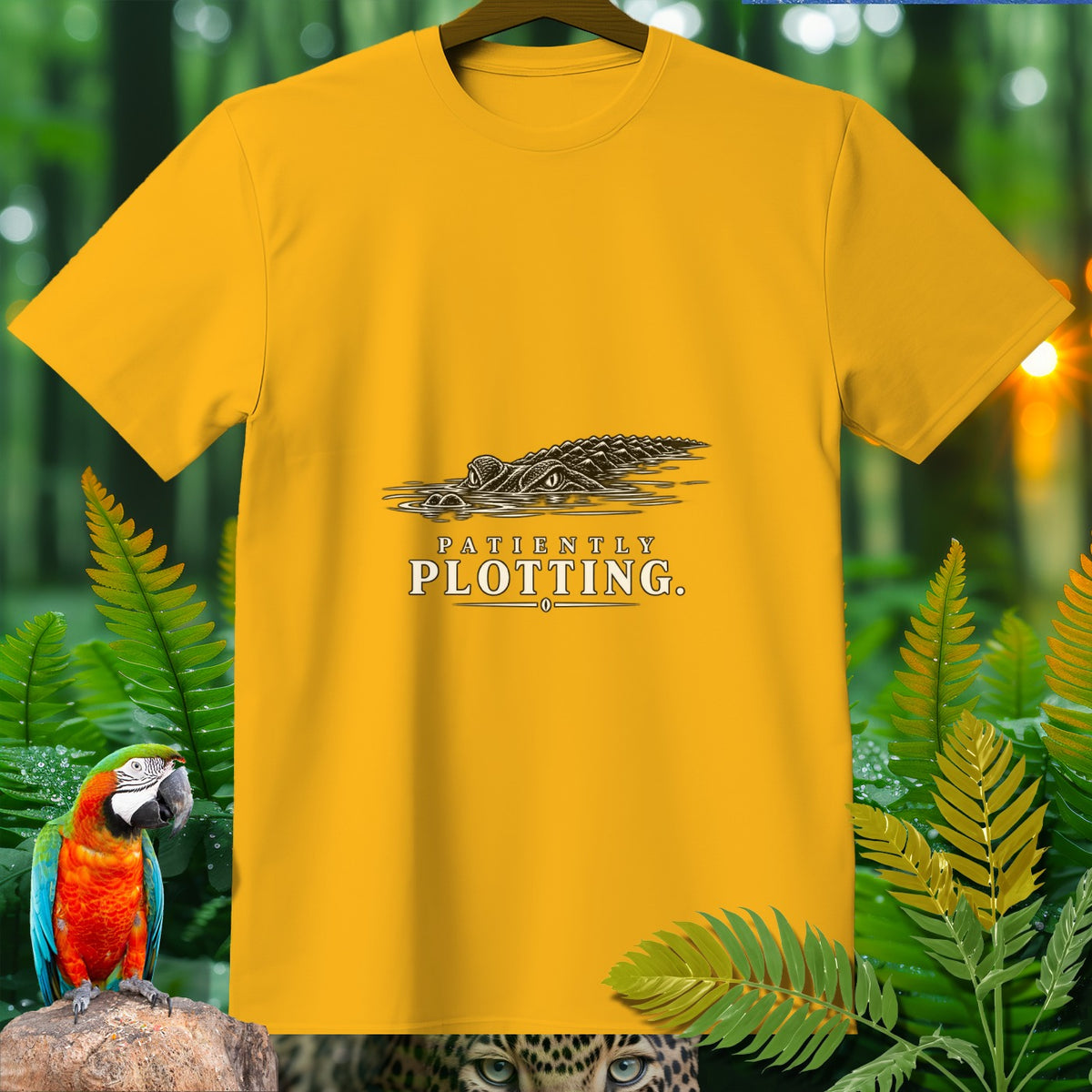 Yellow t-shirt with a graphic of an alligator in water and text reading "PATIENTLY PLOTTING."