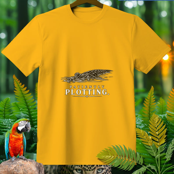 Yellow t-shirt with a graphic of an alligator in water and text reading "PATIENTLY PLOTTING."