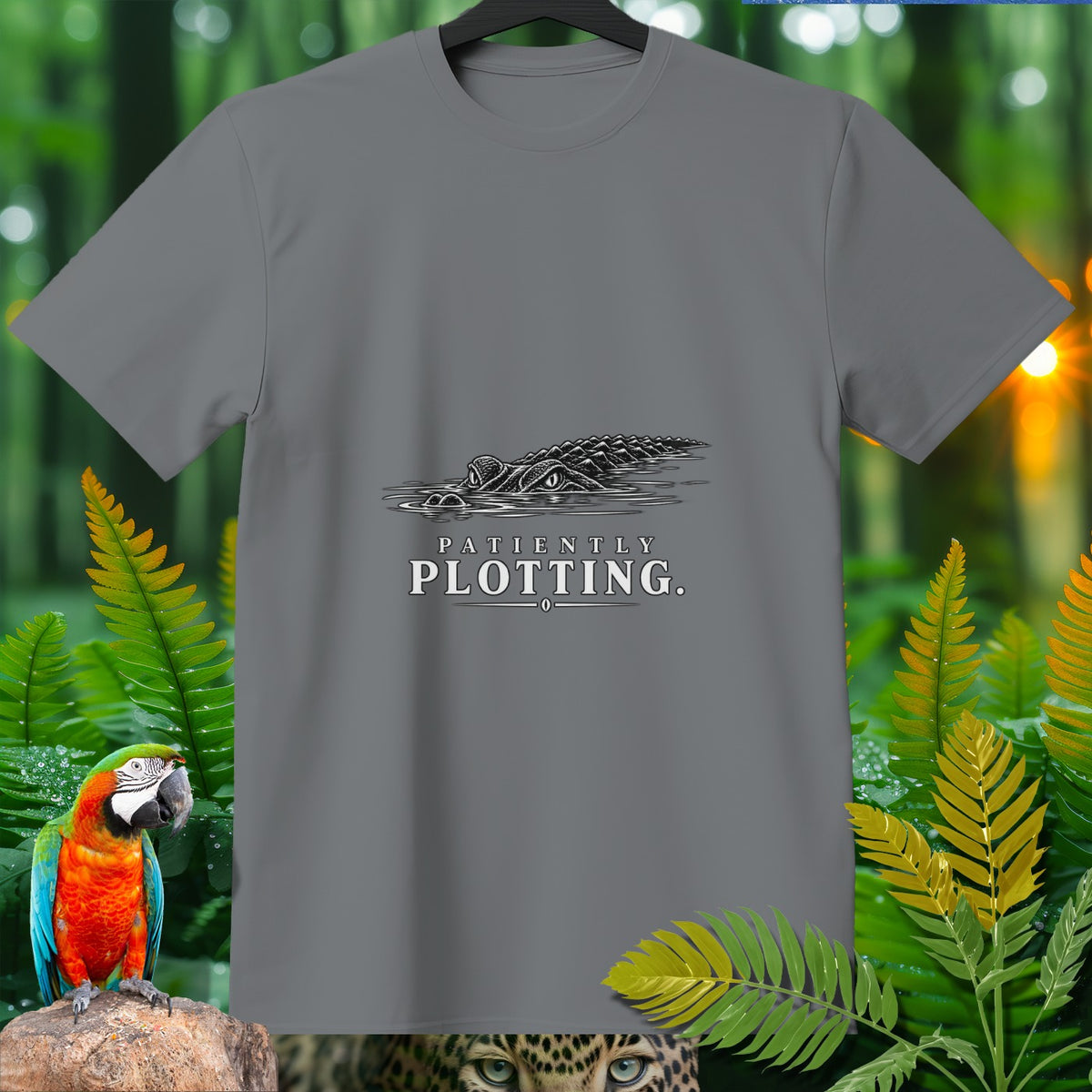 Gray t-shirt with black graphic of an alligator in water, text "Patiently Plotting."