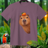 T-shirt with capybara wearing an orange on its head, surrounded by foliage.