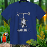 Blue t-shirt with opossum hanging from a branch and text 