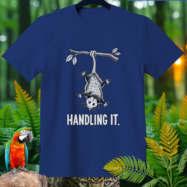 Blue t-shirt with opossum hanging from a branch and text "HANDLING IT."