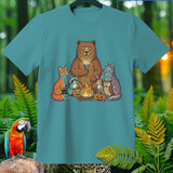Cartoon forest animals gather around a campfire with pumpkins on a teal t-shirt.