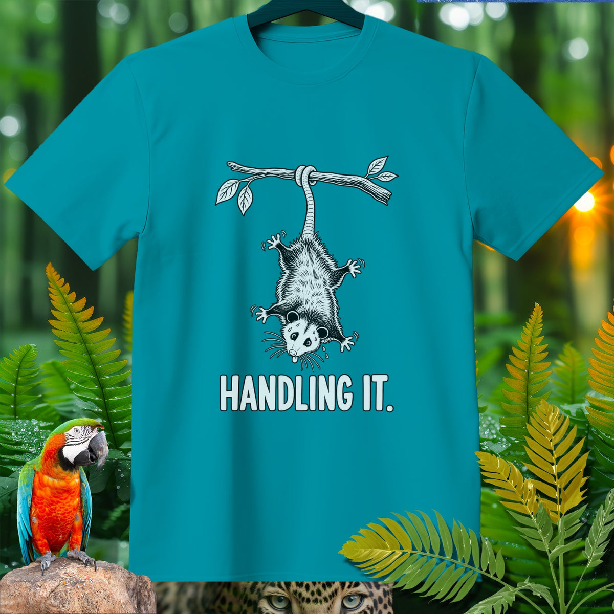 Teal t-shirt with an opossum hanging from a branch, text "HANDLING IT."