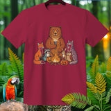 Forest animals gather around a campfire with jack-o'-lanterns on a maroon t-shirt.