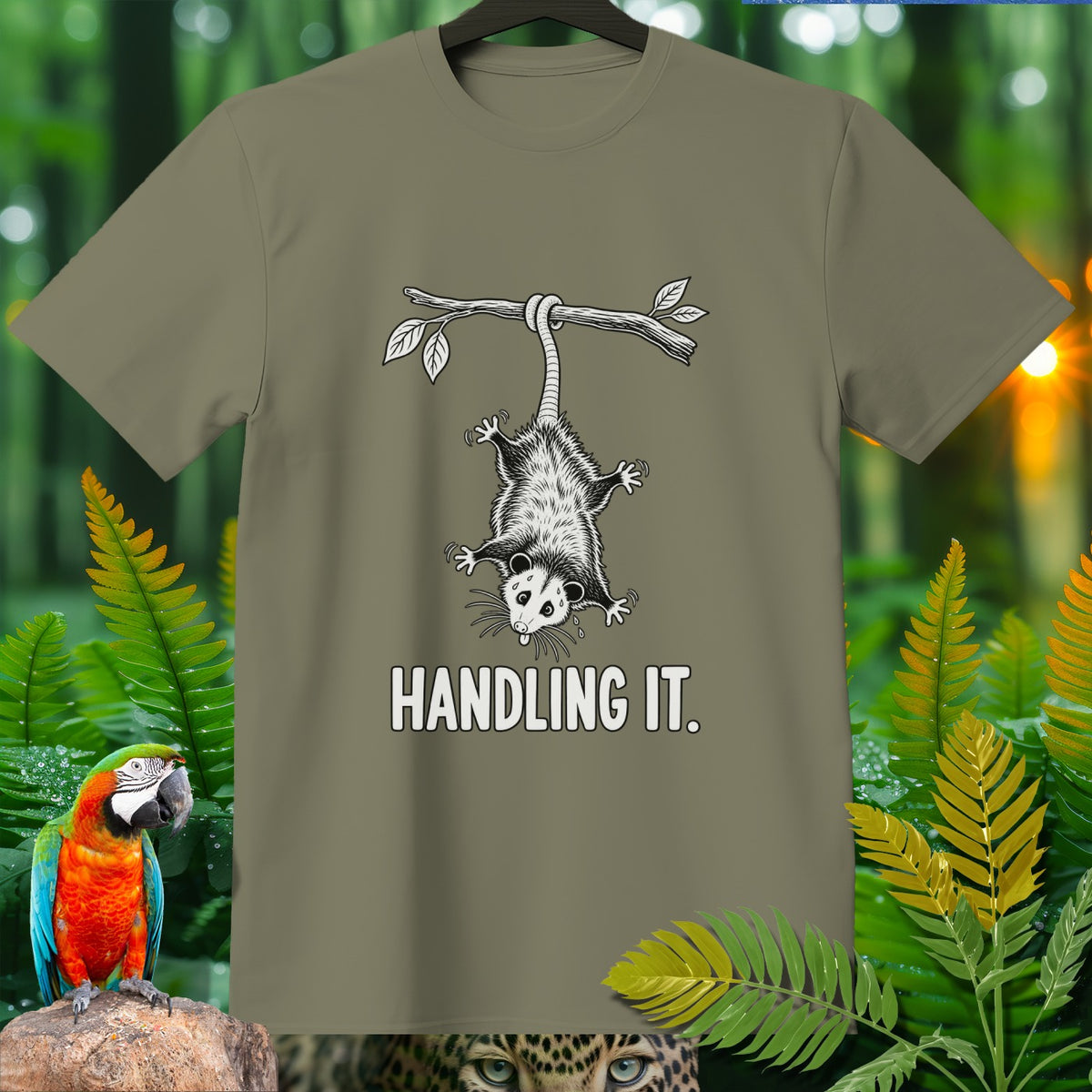 Olive green t-shirt with opossum hanging from branch, text reads "HANDLING IT."