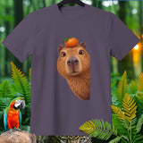 Capybara with orange on head on purple t-shirt, jungle background.