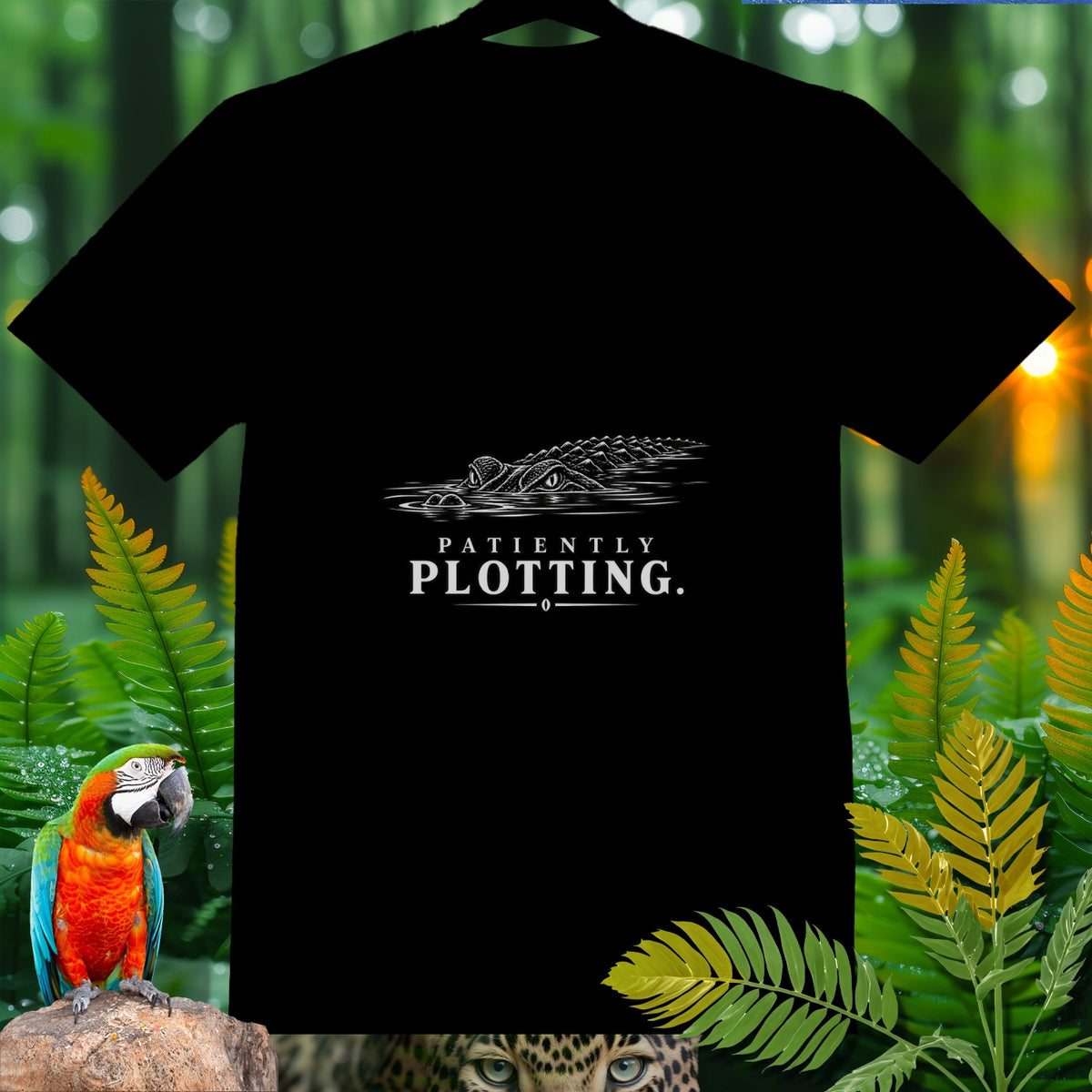 Black t-shirt with white graphic of an alligator and text "PATIENTLY PLOTTING."