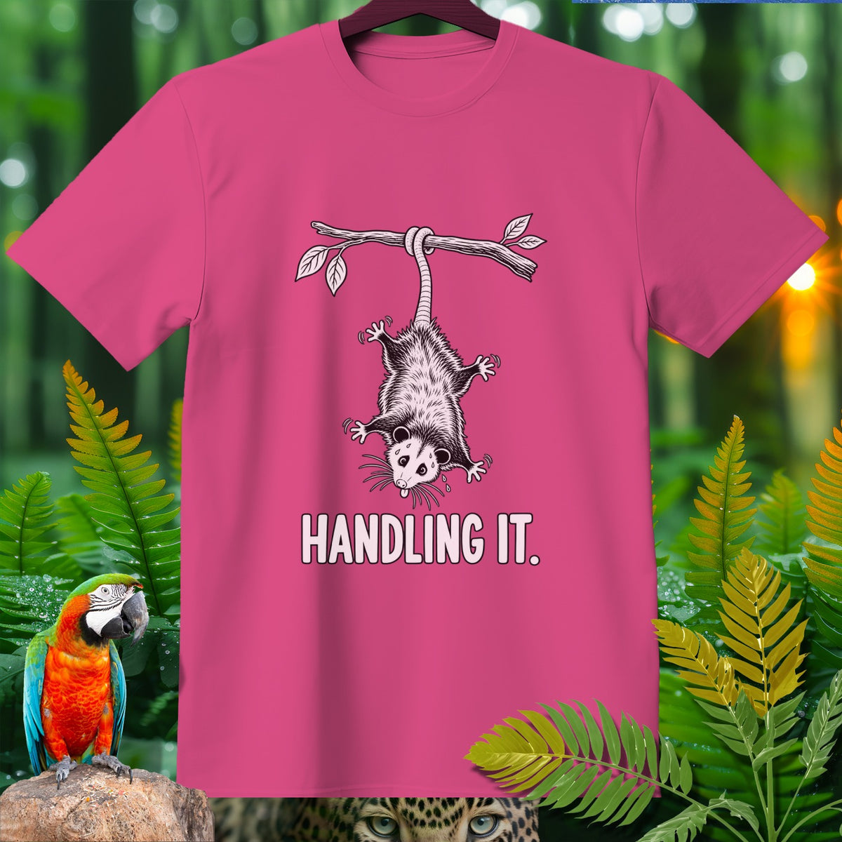 Pink t-shirt with opossum hanging from branch, text "HANDLING IT."