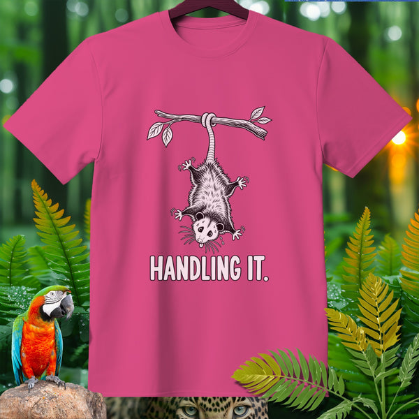 Pink t-shirt with opossum hanging from branch, text "HANDLING IT."