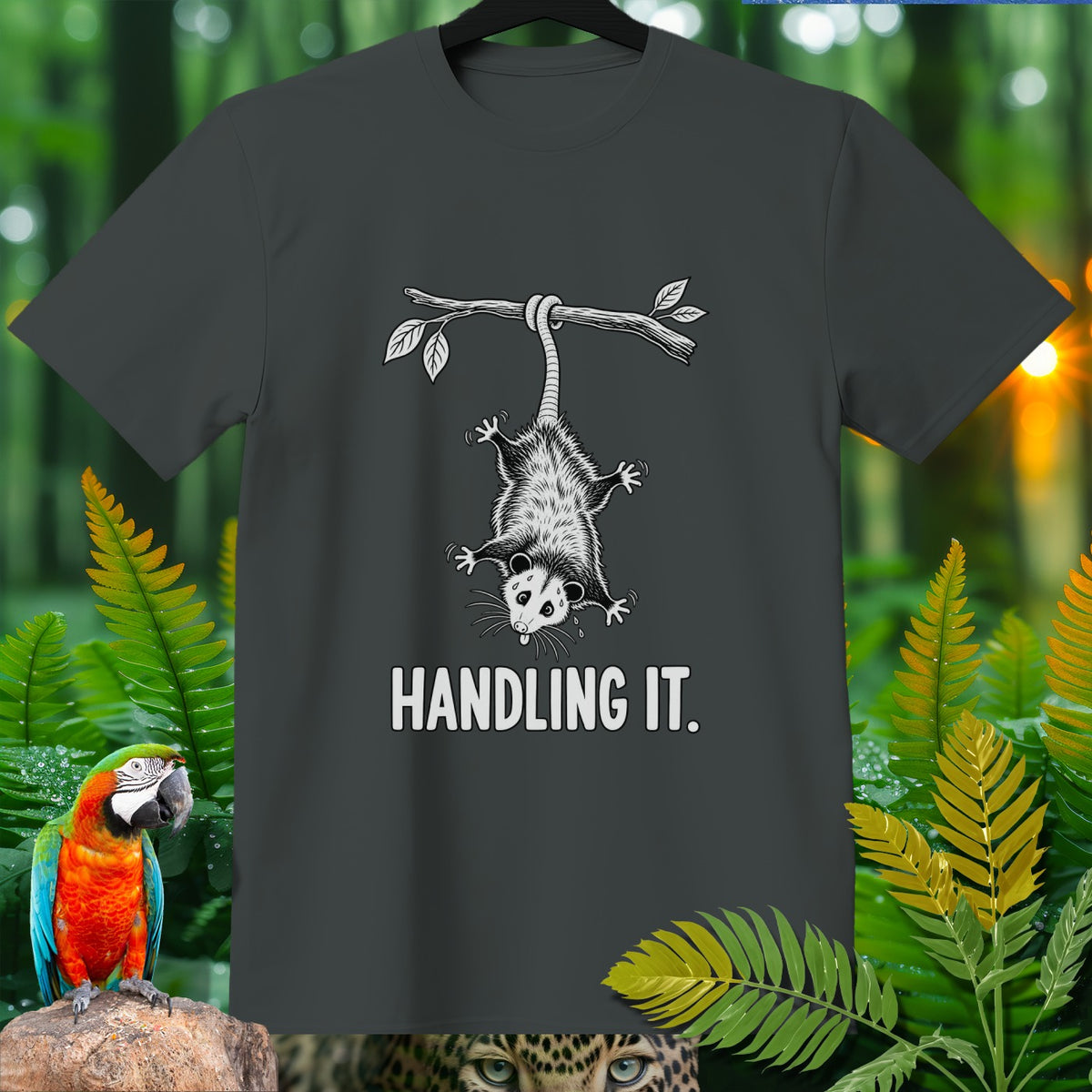 T-shirt with a graphic of an opossum hanging from a branch that says "HANDLING IT."