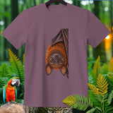 T-shirt with a bat print hanging upside down, surrounded by foliage.